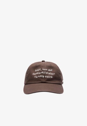 Gorra de béisbol marrón con texto bordado en blanco: "Sonríe, eres la razón por la que alguien sigue adelante."