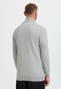 Suéter de punto gris claro con cuello alto, mangas largas y puños acanalados. Terminación con un dobladillo recto y tejido texturizado.