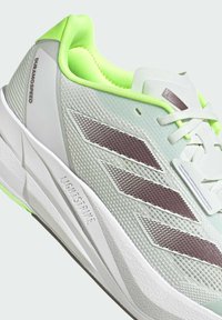 Scarpa da corsa leggera con tomaia in mesh verde menta, dettagli bianchi e verde chiaro, e strisce marroni scure. Dettagli "Lightstrike" sulla suola.