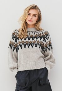 Jasnoszary, dziergany sweter z okrągłym dekoltem, z geometrycznym wzorem w czerni i brązie na wysokości klatki piersiowej. Oversize'owy fason.