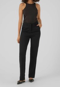 Czarne, dopasowane spodnie z prostą nogawką, z przednimi kieszeniami i gładką, miękką fakturą. W połączeniu z ciemnym, bezrękawnym topem.