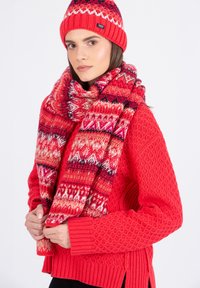 Bonnet et écharpe rouges en tricot avec un motif géométrique, associés à un pull en laine rouge texturé. Tissu doux, design chaleureux et apparence confortable.