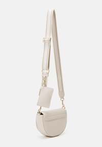 Béžová crossbody taška zaobleného tvaru, vyrobená z hladkého syntetického materiálu, se zlatými kovovými doplňky a odnímatelným držákem na karty připevněným k popruhu.