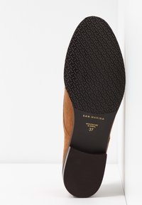 Semelle d'une chaussure en suede marron affichant un traçage texturé noir, marque "SAN MARINA", "Fabriqué au Brésil", et taille 37 en lettres dorées.