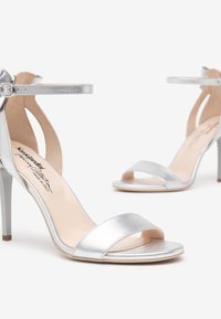 Sandales à talons hauts argentées avec une finition brillante, une bride de cheville et un design à bout ouvert avec des détails découpés élégants.