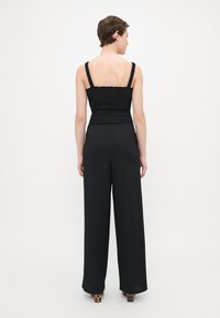 Zwarte gesmokte mouwloze top gecombineerd met zwarte wijde broek, met een textuurstof en dierenprint hakken.