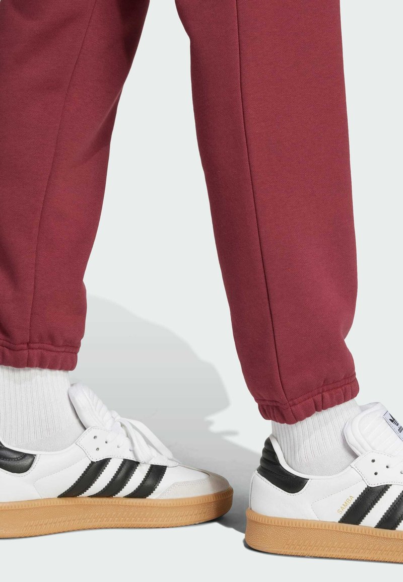 Fehér bőr sneakers fekete csíkokkal, rágó talppal, bordó melegítőnadrággal, amely elasztikus mandzsettákkal és puha tapintással rendelkezik.