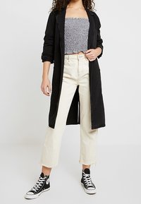Sort lang frakke over en smocked strapless top, parret med off-white cropped jeans og sorte høj-top sneakers med hvide såler.