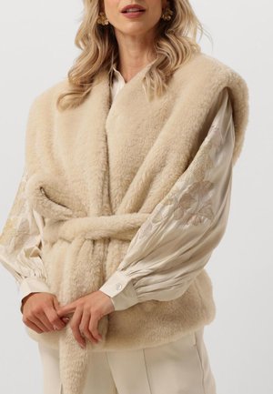 Beige nepbontvest met een wikkeldesign, voorzien van een ceintuur in de taille. Versierde, gepatterneerde mouwen in een lichte stof voegen contrast toe.