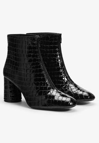 Botines negros de tobillo hechos de material con relieve de cocodrilo brillante, con cierre de cremallera, punta afilada y tacón grueso.