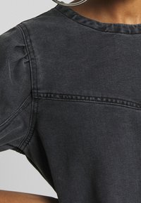 Svart denim topp med puffärmar, rund halsringning och subtila sömnadsdetaljer framtill och baktill för extra struktur.