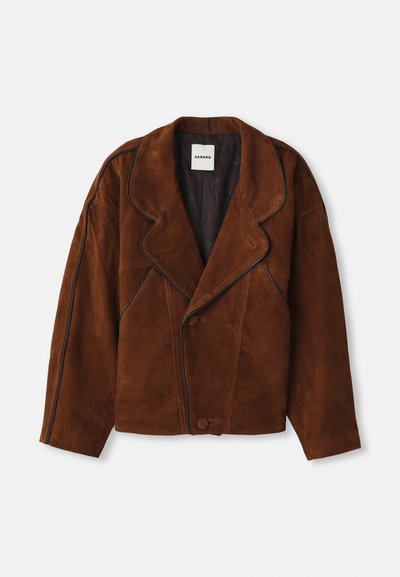 Giacca in suede marrone con colletto a punta, vestibilità over-size, chiusura doppiopetto e piping a contrasto lungo le cuciture.