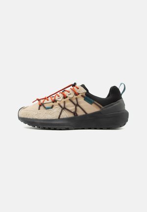 Beżowo-czarny sneaker z pomarańczowymi i brązowymi sznurówkami, teksturowanym przodem, grubą czarną podeszwą i turkusową pętelką na pięcie.
