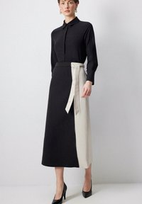 Robe chemise noire à manches longues avec un col, associée à une jupe taille haute avec une ceinture crème contrastante et des talons noirs élégants.