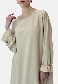 Beiges Kleid aus glattem Stoff mit rundem Ausschnitt und gerafften Ärmeln. Es hat eine lässige Passform und eine sanft ausgestellte Silhouette.