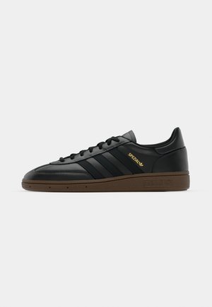 Black leather sneaker with three dark stripes, gold "Spezial" logo, and brown rubber sole; smooth texture with rounded toe design.