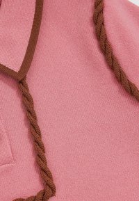 Roosa kootud kangas pruuni punutud detailiga kaela ääres. Omab tekstuurset pinda ja ühtlast värvitooni.