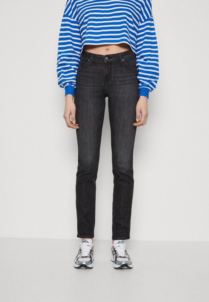 Jean skinny noir à taille mi-haute, associé à un pull court rayé bleu et blanc. Le mannequin porte des baskets argentées et noires.