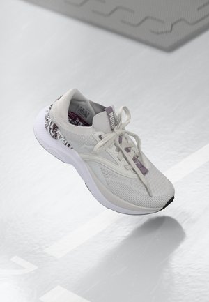 White sneaker with textured knit upper, purple accents, and solid rubber outsole. Features laces and a patterned heel design.