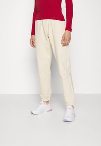 Pantalones de chándal color crema, ajustados en la parte inferior con cintura elástica y puños, combinados con zapatillas deportivas blancas que tienen acentos en rosa y morado.