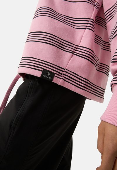 Rosa gestreifter Sweatshirt mit schwarzen horizontalen Linien, ausgestattet mit einem gerippten Bündchen und einem Etikett mit der Aufschrift "FIRE + ICE." Kombiniert mit schwarzen Stoffhosen.