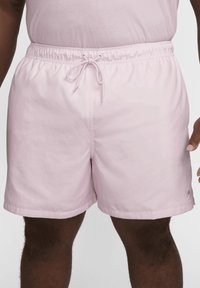 Shorts de bain rose clair en tissu léger. Dotés d'une taille élastique avec un cordon de serrage et d'un petit logo en bas à gauche.