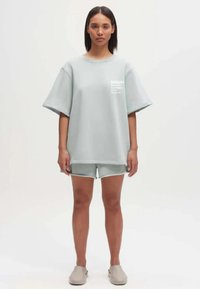 Oversized lichtgrijze katoenen t-shirt met korte mouwen en logo, gecombineerd met bijpassende shorts. Heeft een ontspannen pasvorm en een gladde textuur.