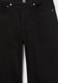 Czarne dżinsy z denimu z przednimi kieszeniami, miedzianymi nitami i srebrnym guzikiem, widoczne od talii do połowy uda.