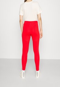 Červené legíny s hladkou texturou, s bílými bočními pruhy, spárované se světle šedým tričkem a bílými teniskami.