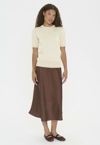 Beige short-sleeve sweater, brown mid-length skirt, smooth texture. Brown flats with tie accents. Simple, fitted design.
