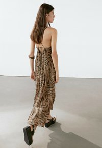 Robe maxi à rayures brunes et noires avec un design à encolure halter, dos nu et tissu fluide ; associée à des sandales à plateforme noires.