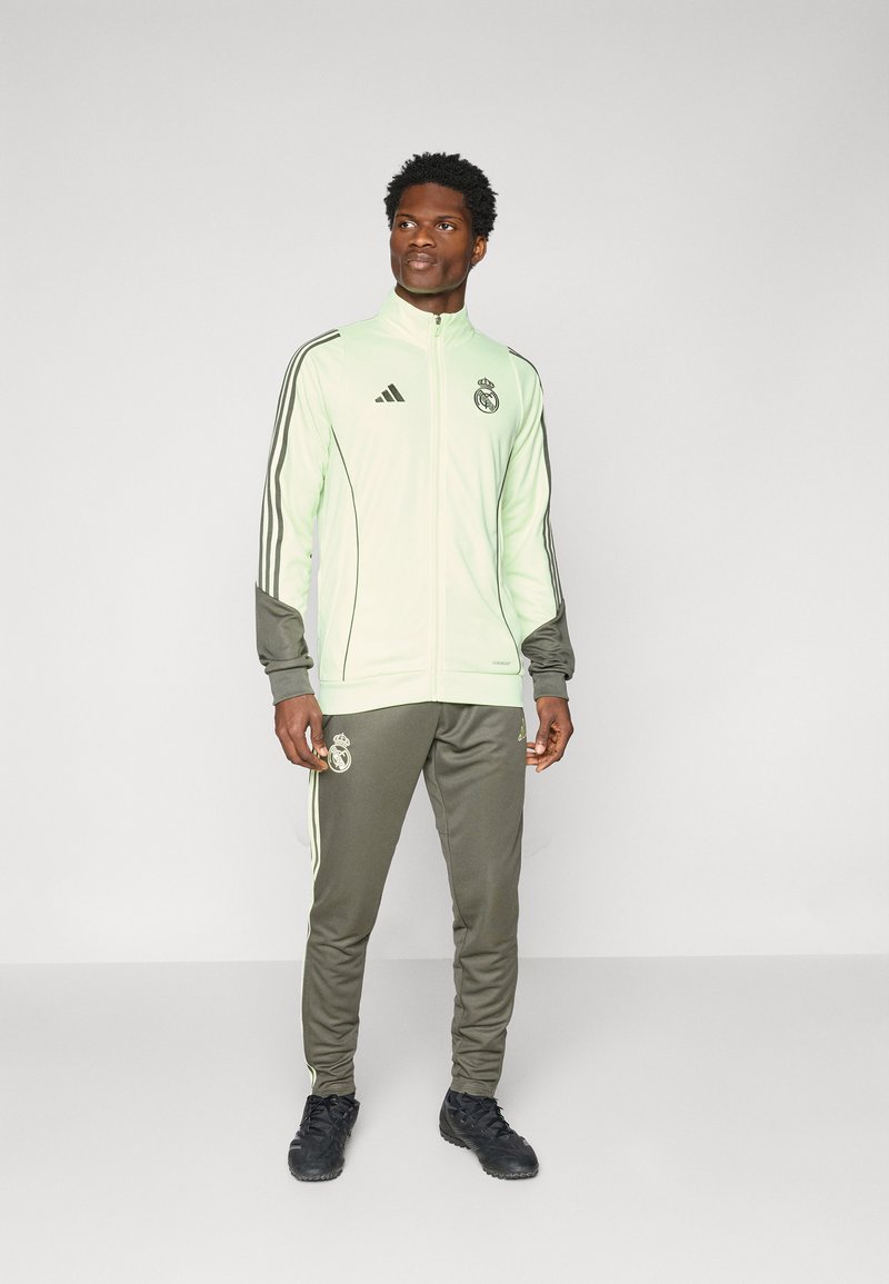 Light green athletic tracksuit with gray accents. Features zip-up jacket with black logo and matching tapered pants, made of smooth fabric.