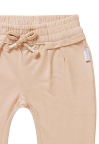 Zachte perzikkleurige joggers van stof met een elastieken tailleband met een trekkoord, zijzakken en gestikte details. Kleine merketiket aan de zijkant.