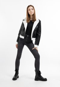 Sort læderjakke med hvid shearlingkrave, tætsiddende sort top og højtaljede mørke jeans. Modellen har sorte hæl-snørede kampstøvler på.