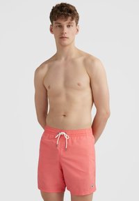 Maillots de bain corail avec taille élastique et cordon de serrage, arborant un petit logo sur la jambe inférieure et un tissu lisse et léger.
