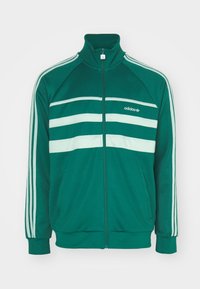 Grön Adidas zip-up sportjacka med vita ränder på ärmarna och bröstet, hög krage och sidofickor.