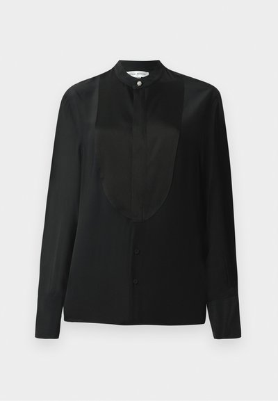 Maglietta nera a maniche lunghe in tessuto morbido, con colletto alto, una pattina con bottoni e un dettaglio in pannello liscio lungo la parte frontale.