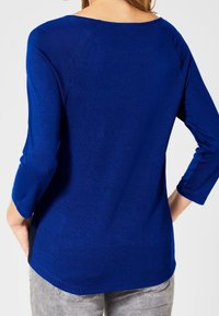 Haut bleu à manches longues avec un décolleté arrondi et une silhouette légèrement ajustée. Le matériau semble doux, lisse et léger.