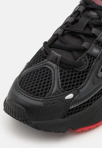 Czarne sneakersy wykonane z siateczki i sztucznej skóry, z teksturowanymi detalami, kontrastującymi czerwonymi akcentami oraz wyściełanym kołnierzem.