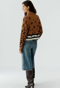 Bruine luipaardprint trui met een geribde kraag, gedragen met blauwe wijde jeans. Zachte textuur en contrasterende gestreepte onderrand.