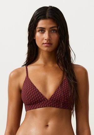 Junge Frau mit langen, nassen Haaren, die ein strukturiertes, braun-rotes Bikinioberteil mit Dreiecksmuster vor einem schlichten hellen Hintergrund trägt.