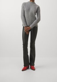 Maglione grigio a coste, pantaloni di pelle neri a zampa d'elefante e stivali rossi con tacco e borchie. Focus sulla texture e sui colori contrastanti.