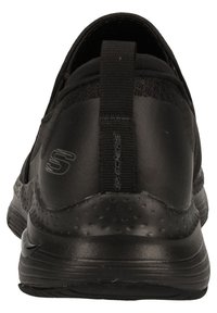 Zapatilla deportiva negra tipo slip-on con parte superior texturizada, talón mate liso y suela texturizada para tracción. Logo grabado en el lateral.