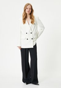 Dobbeltbrystet hvid blazer med sorte knapper, notched klapkraver og sidelommer, parret med højrejsede sorte bukser.