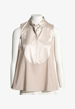 Blouse beige sans manches avec bavette en satin à l'avant, col boutonné et coupe ample et fluide, présentée sur un torse de mannequin blanc.