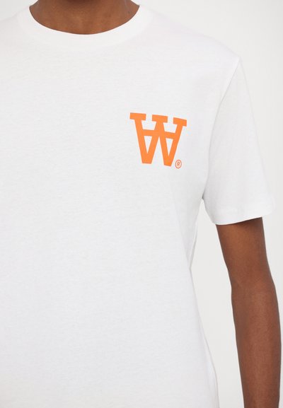 Hvid bomulds t-shirt med et lille orange grafik af omvendte bogstaver "W" og "A" på venstre brystområde. Kortærmet, rund hals design.