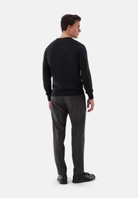 Schwarzer Strickpullover mit rundem Halsausschnitt, kombiniert mit dunkelbraunen strukturierten Hosen und schwarzen Schuhen. Einfaches, figurbetontes Design mit langen Ärmeln.