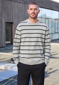 Ljusgrå tröja med svarta horisontella ränder, ribbade ärmslut och nederkant, rund halsringning, matchad med mörka byxor. Slät stickad textur.