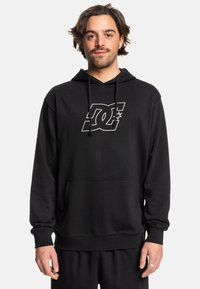 Sudadera negra de tela suave, con un bolsillo canguro en la parte frontal y capucha con cordones. Gran logo de DC impreso en blanco en el pecho.