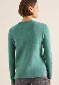 Maglione turchese a maglia con maniche lunghe, polsini e orlo a coste, caratterizzato da un motivo testurizzato lungo i lati. Tessuto morbido di peso medio.